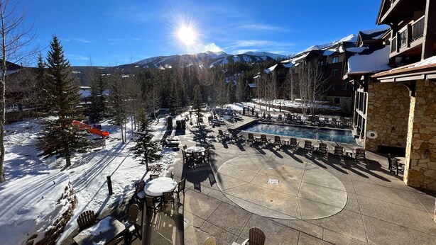 Ein Resort mit Außenbestuhlung und Pool, umgeben von schneebedeckten Bergen und Bäumen.