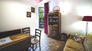 A dining area with a wooden table and chairs, a cabinet with glassware, a red curtain, and a view through a window.