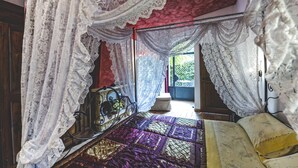 A bedroom with a bed, a nightstand, and a window with lace curtains.
