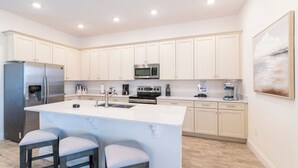 A modern kitchen with white cabinets, stainless steel appliances, a central island with bar stools, and a painting on the wall.