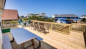 Una terraza de madera con una mesa y sillas, con vista a una playa y casas al fondo.