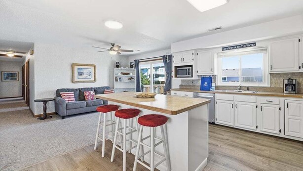Una cocina moderna con armarios blancos, una isla central con taburetes, un ventilador de techo y vistas al exterior a través de una ventana.