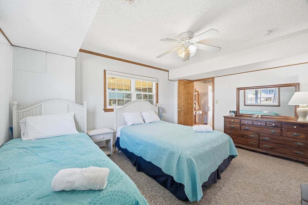 A bedroom with two beds, a ceiling fan, a wooden dresser, and a window.