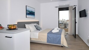A modern hotel room with a bed, a bedside table with a fruit bowl, a TV mounted on the wall, and a balcony with a railing. - Economic Studios B9 (Iraklion Crete)