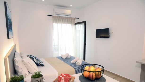 A hotel room with a bed, a bedside table with a fruit bowl, a small plant, and a tray of magazines. - Economic Studios B9 (Iraklion Crete)