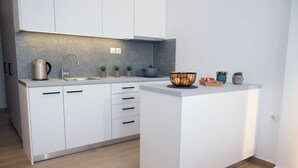 A modern kitchen with white cabinets, a stainless steel kettle, a sink, and a countertop with potted plants and a fruit bowl. - Economic Studios B9 (Iraklion Crete)