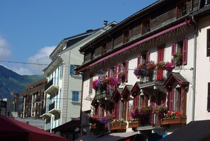 A traditional building with balconies adorned with colorful flowers, a mountainous backdrop, and a clear sky.