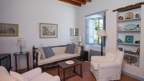 A living room with a sofa, armchairs, a coffee table, and a TV. There are framed pictures on the wall, a lamp, and a shelf with decorative items. - Traditional villa in Hora with sea view to the Aegean  (ΠΑΤΜΟΣ)