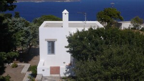 A white building with a small window and a chimney, surrounded by trees and overlooking a body of water. - Traditional villa in Hora with sea view to the Aegean  (ΠΑΤΜΟΣ)