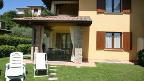 Uma casa de dois andares com varanda coberta, pilares de pedra e área de jantar com mobiliário para exterior.
