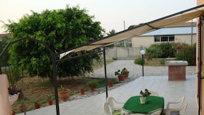 Eine Terrasse im Freien mit Tisch und Stühlen, umgeben von Topfpflanzen und einer Pergola.