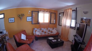Ein Wohnzimmer mit orangefarbenen Wänden, einem Sofa, zwei Sesseln, einem Couchtisch und einem Fernseher.