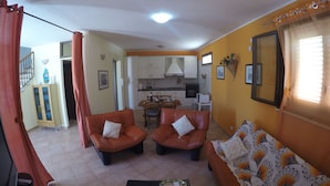 Ein Wohnzimmer mit einer Couch, zwei Sesseln, einem Couchtisch und einem Essbereich mit Tisch und Stühlen.
