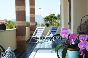 A balcony with lounge chairs, a glass table, and potted orchids. - Casa Eleatica is a modern and comfortable house in the center of Ascea Marina (Marina di Ascea)