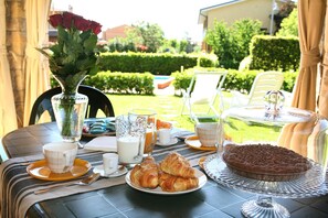 A breakfast table with croissants, a pie, and a vase of flowers.