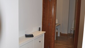 Un pasillo con suelo de madera, un aparador blanco con cajones y una puerta que da a otra habitación.