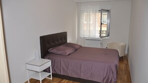Un dormitorio con cama, mesita de noche, una silla y ventana con cortinas.