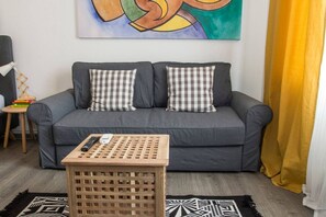 Ein graues Sofa mit karierten Kissen, ein Couchtisch aus Holz mit Fernbedienung und ein gemustertes Teppich.