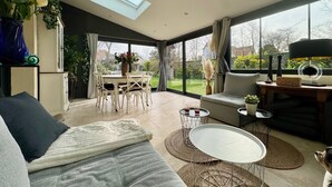 A spacious living area with a high ceiling, a skylight, a dining area with a table and chairs, and a view of the outdoors.