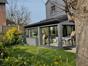 Une maison moderne dotée d’une véranda en verre, d’un mur en briques et d’un jardin bien entretenu.
