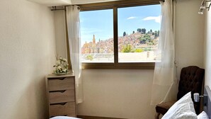 A bedroom with a bed, a nightstand, a dresser, a window with curtains, and a view of a cityscape. - Wonderful sea view - Santa Maria (Menton)