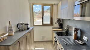 A modern kitchen with wooden cabinets, a built-in oven, a coffee maker, and a window with a view of buildings. - Wonderful sea view - Santa Maria (Menton)