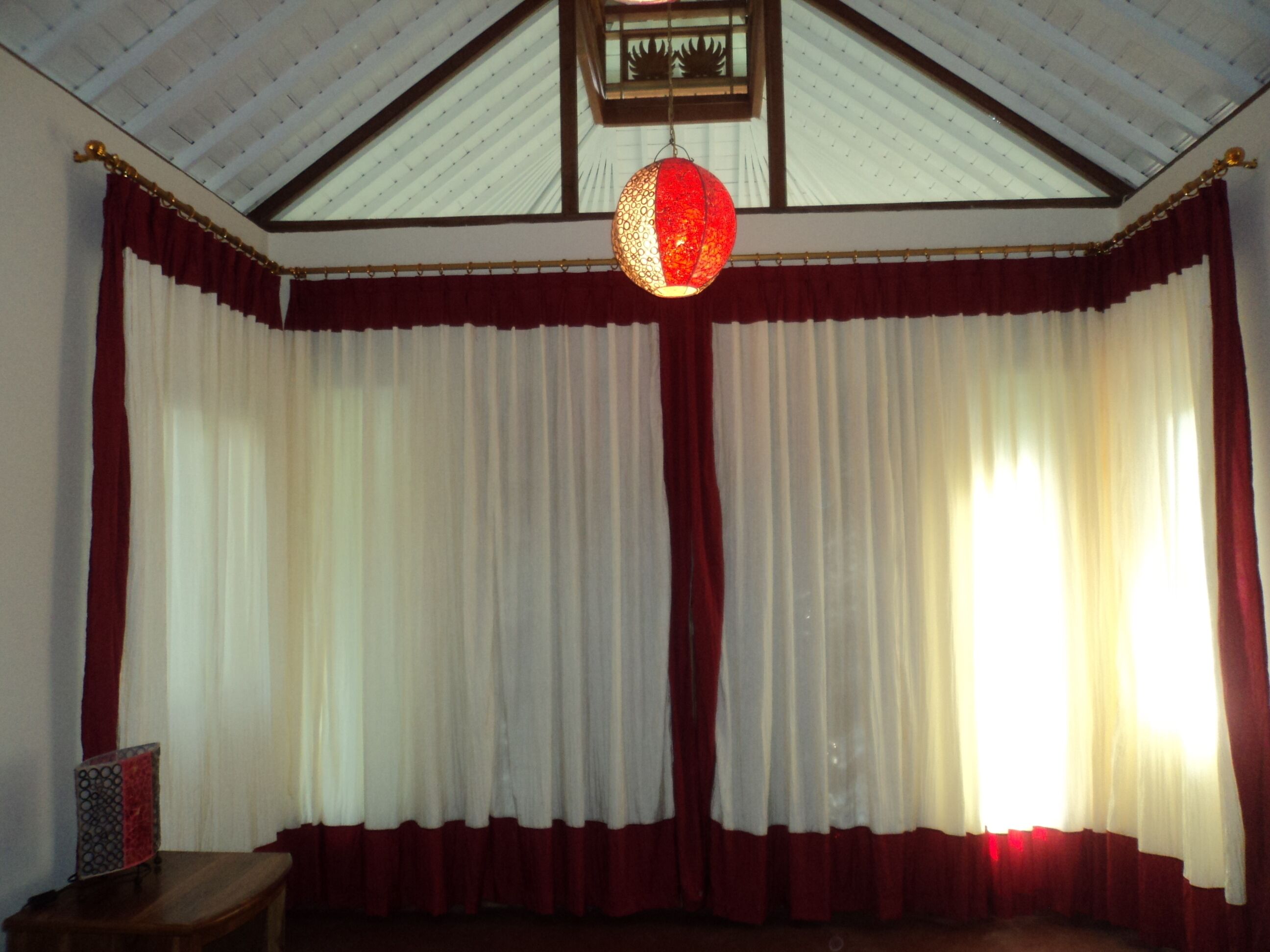 A room with a high ceiling, large windows with red and white curtains, and a hanging lantern.