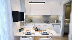 A modern kitchen with white cabinets, a flat-screen TV, a coffee maker, and a breakfast setup with croissants and orange juice. - Economic Studio B10 (Iraklio)