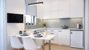 A modern kitchen with white cabinetry, a flat-screen TV mounted above the counter, and a small refrigerator. - Economic Studio B10 (Iraklio)