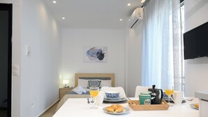 A hotel room with a bed, a breakfast table with croissants, a coffee maker, and a TV on the wall. - Economic Studio B10 (Iraklio)