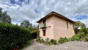 Une maison à deux étages avec un balcon, entourée de verdure et bordée d’un chemin pavé.