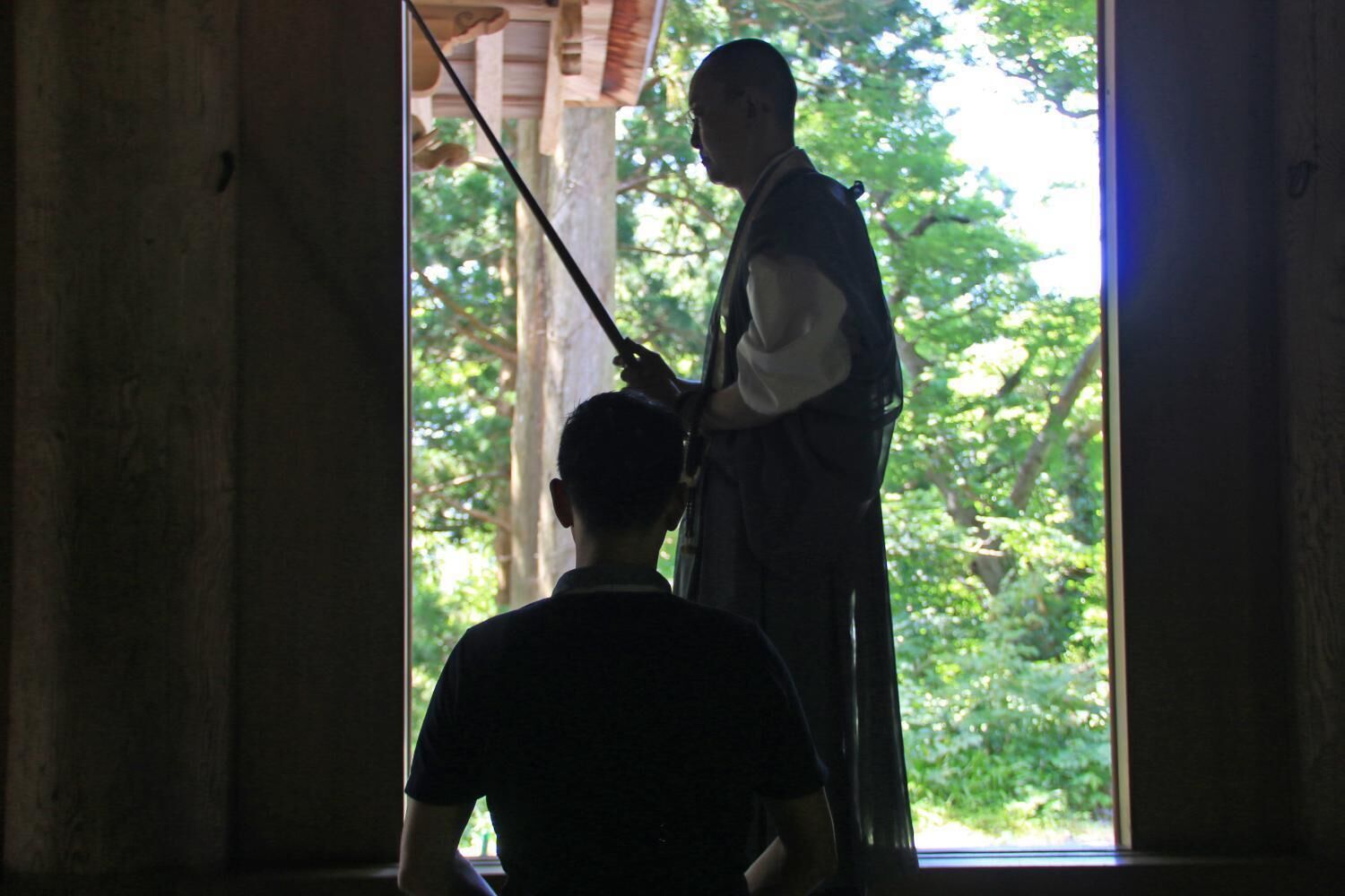 A person standing in a doorway with a long object, possibly a tool, in their hand.