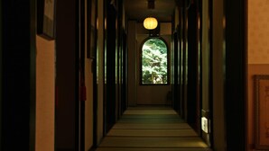 A narrow hallway with a wooden floor, a hanging lantern, and a window with a view of trees.