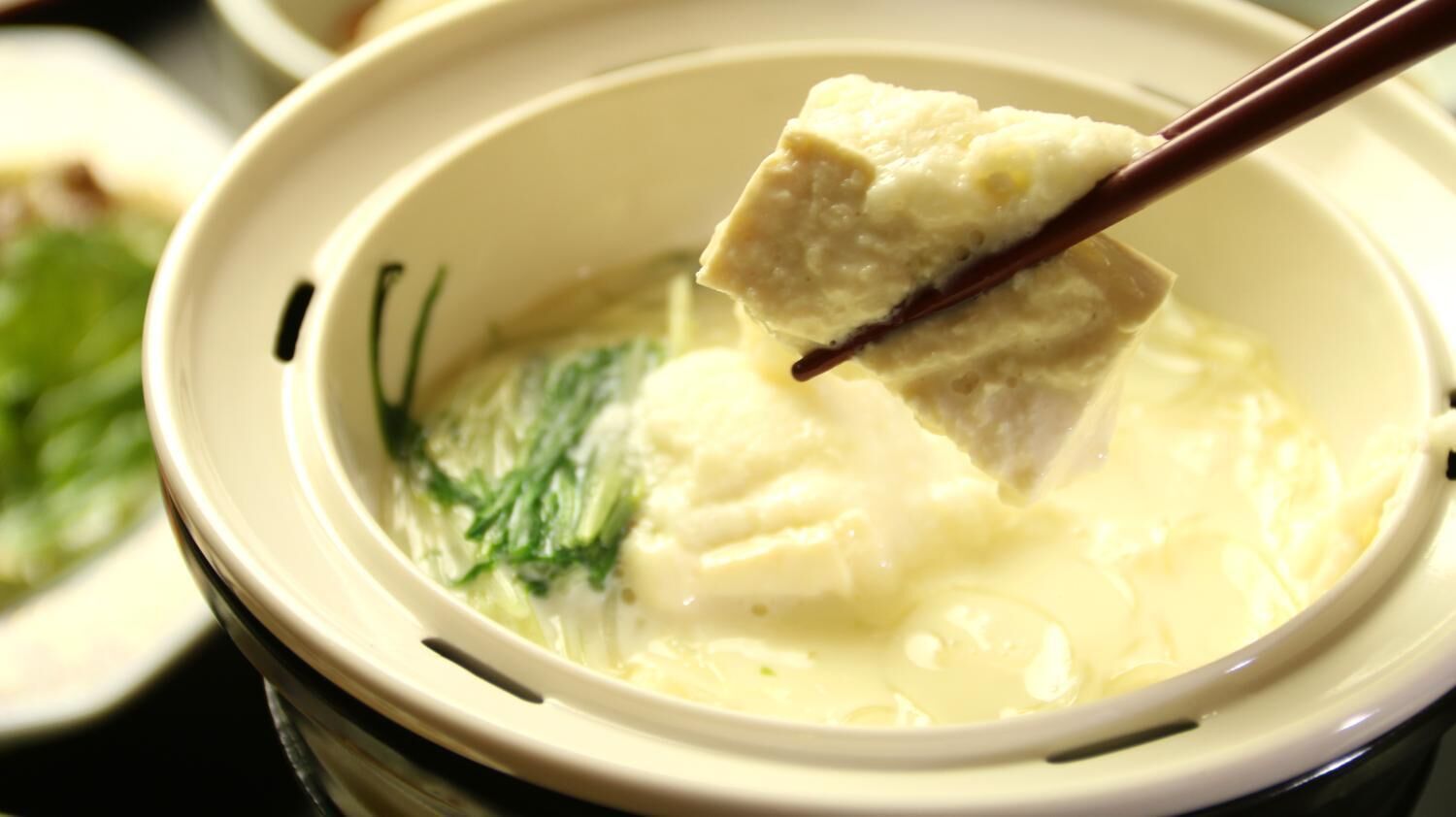 A bowl of soup with a piece of tofu being lifted by chopsticks.