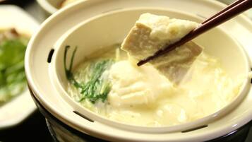 A bowl of soup with a piece of tofu being lifted by chopsticks.