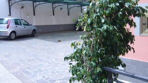 A parking area with a white car, a stone-paved ground, and a building with a pink wall and a green awning. - Palinuro home 'Donna Antonia' (Palinuro)