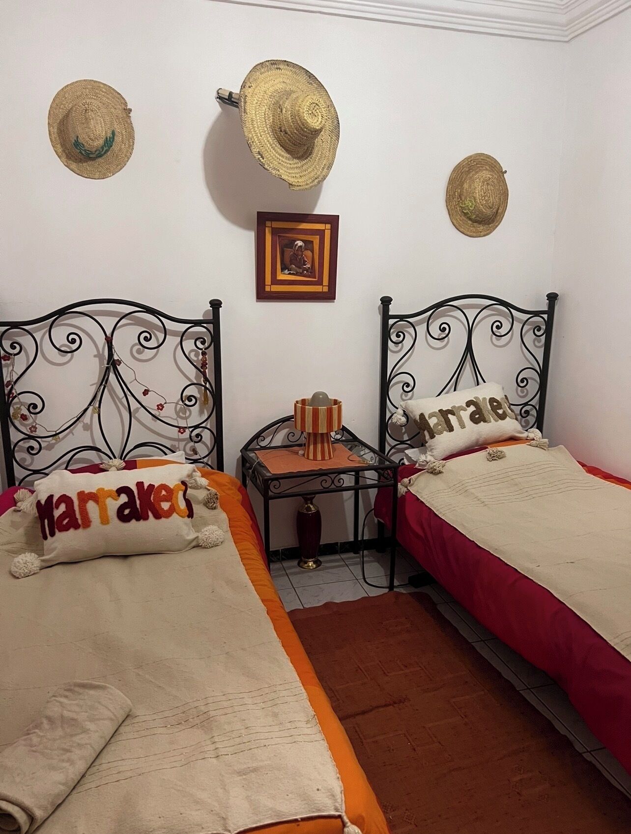 Una habitación con dos camas, una mesita con una lámpara y dos sombreros colgados en la pared.