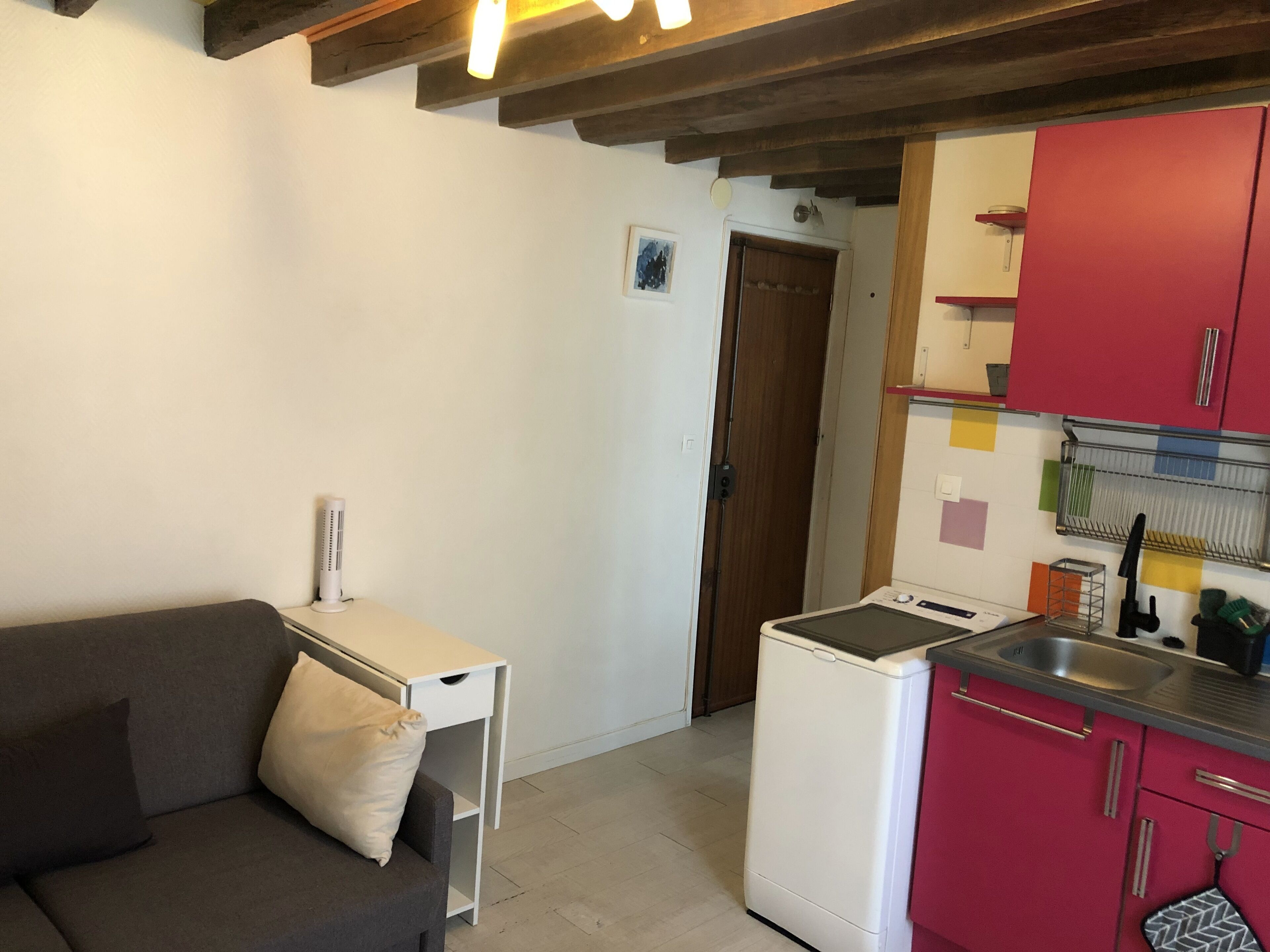 Un espace de vie compact comprenant un canapé, une petite table, un appareil électroménager blanc et une kitchenette dotée de meubles rouges.