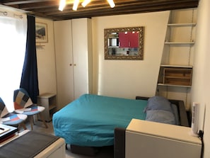 A bedroom with a bed, a desk, a chair, a small table, a mirror, and a wardrobe. - Beautiful studio, 1 or 2 people (Paris)