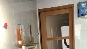 Une salle de bain avec un mur recouvert de carreaux blancs, une porte en bois avec des panneaux de verre, un radiateur et une étagère contenant des articles de toilette.