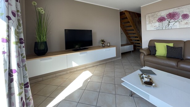 A living room with a flat-screen TV, a sofa, a coffee table, and a staircase. - COMPLETELY RENOVATED! NO PRICE INCREASE FOR 2026+2027 !!! BEACH CHAIR INCLUDED! (Binz)