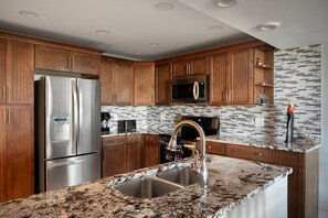 A modern kitchen with wooden cabinets, stainless steel appliances, a granite countertop, and a tiled backsplash.