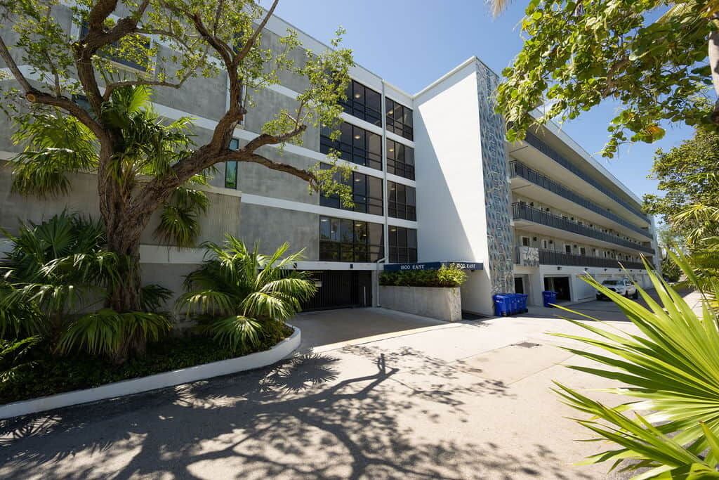 A modern building with a multi-story structure, large windows, and a parking area with blue bins.