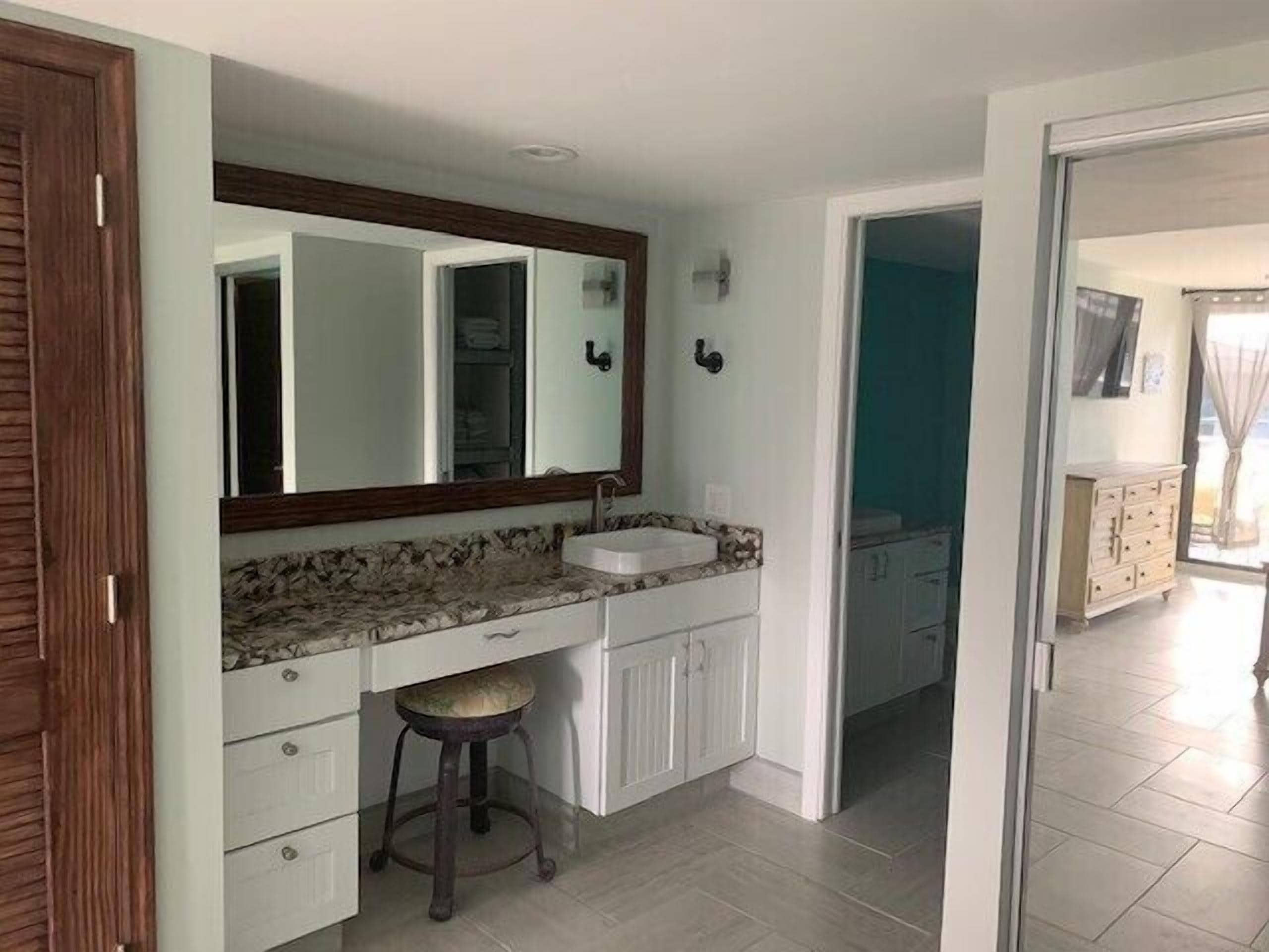 A bathroom with a white vanity, a sink, a mirror, and a stool.