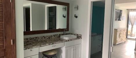A bathroom with a white vanity, a sink, a mirror, and a stool.