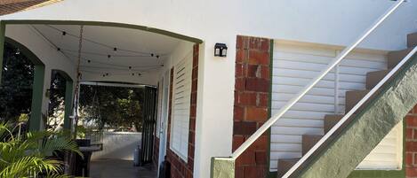 Un espace extérieur abrité, doté d’un escalier menant à un deuxième étage, d’un mur en briques et d’une porte de garage blanche.
