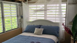 Ein Schlafzimmer mit Bett, einem Fenster mit Jalousien und einer Pflanze.