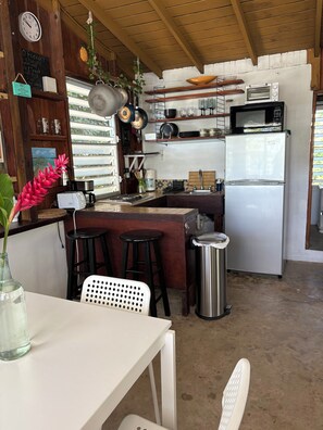 A kitchen with a refrigerator, microwave, and stove. There are stools and a table with a vase.