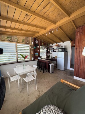 A compact kitchen with wooden beams, a dining area with white chairs, and a small bar area.