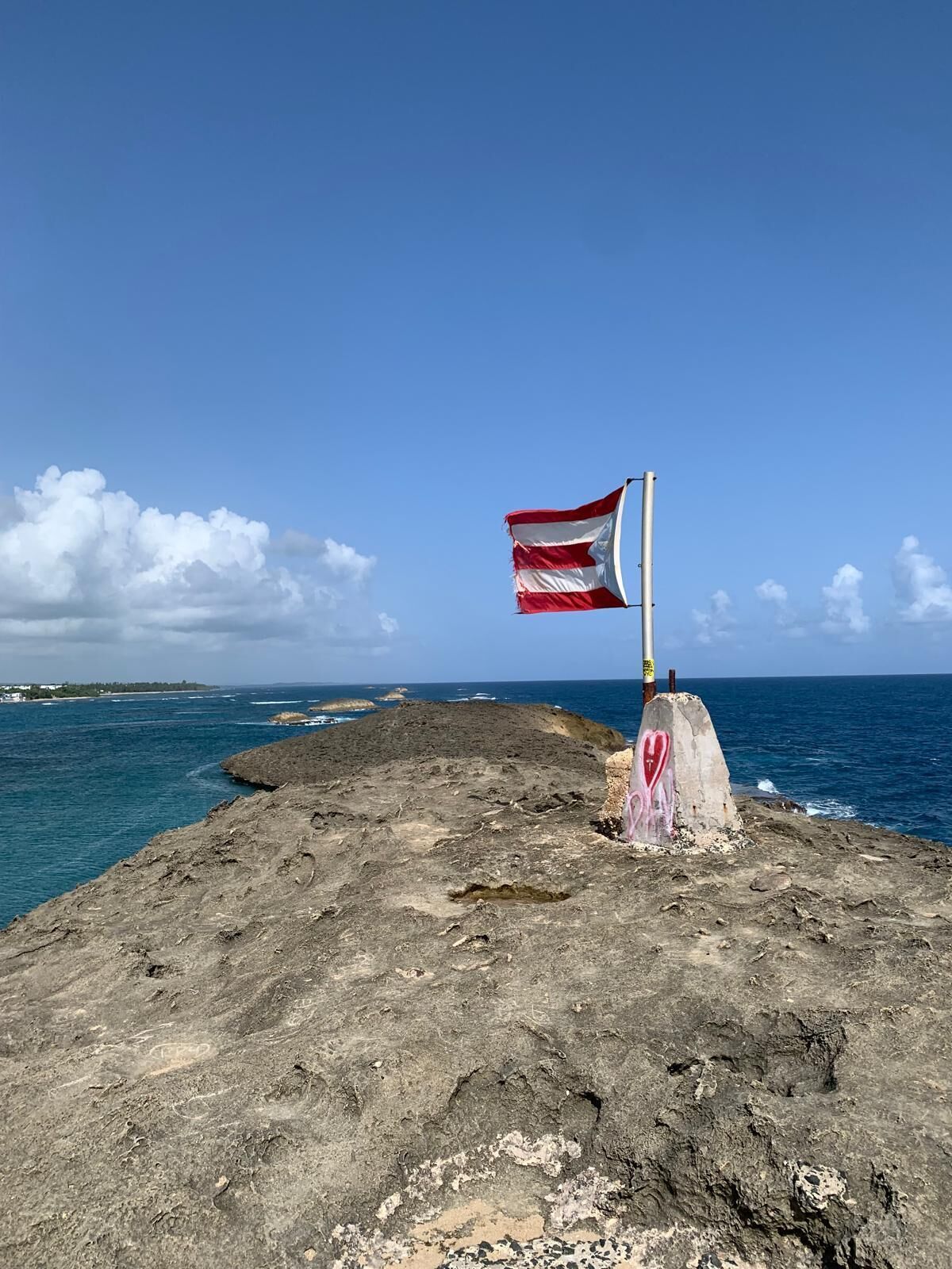 A flagpole with a flag on a rocky coastline.